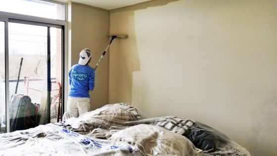 Man wearing a blue shirt painting a wall beige