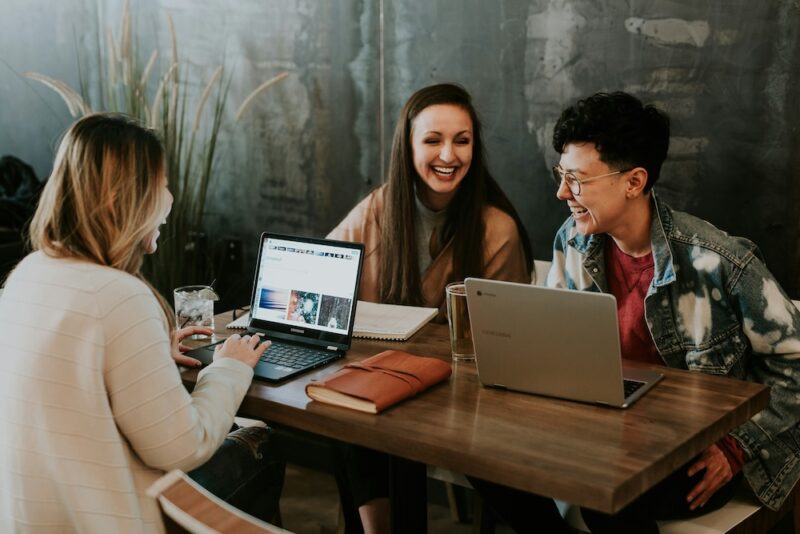 3 friends sitting at a table on their computers laughing